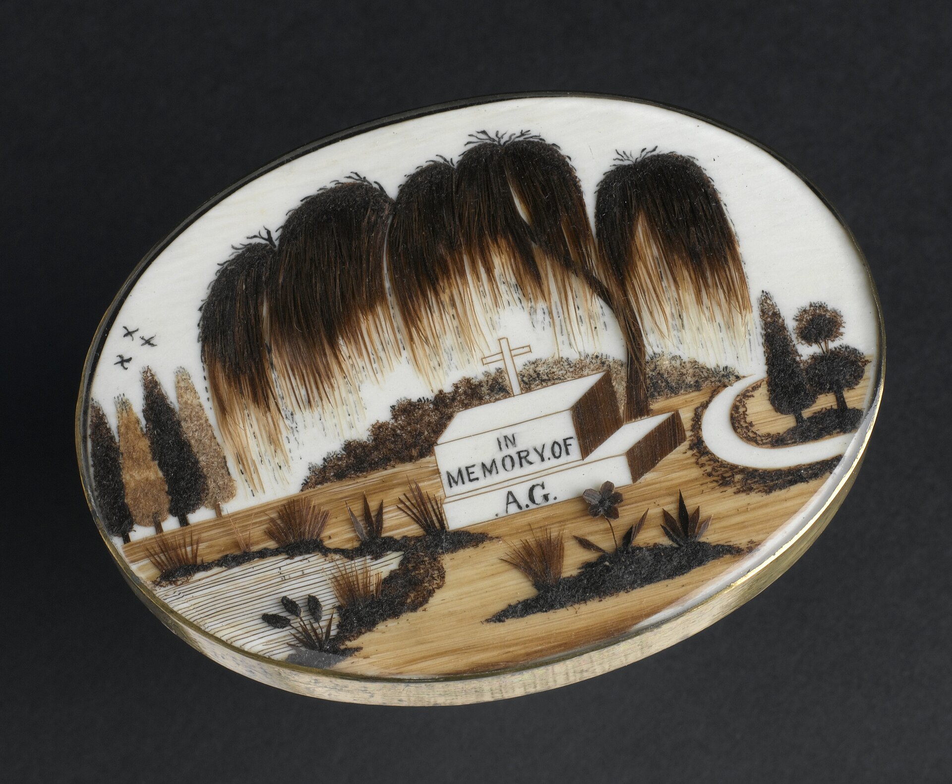 Memorial brooch containing a graveyard scene made from human hair beneath glass